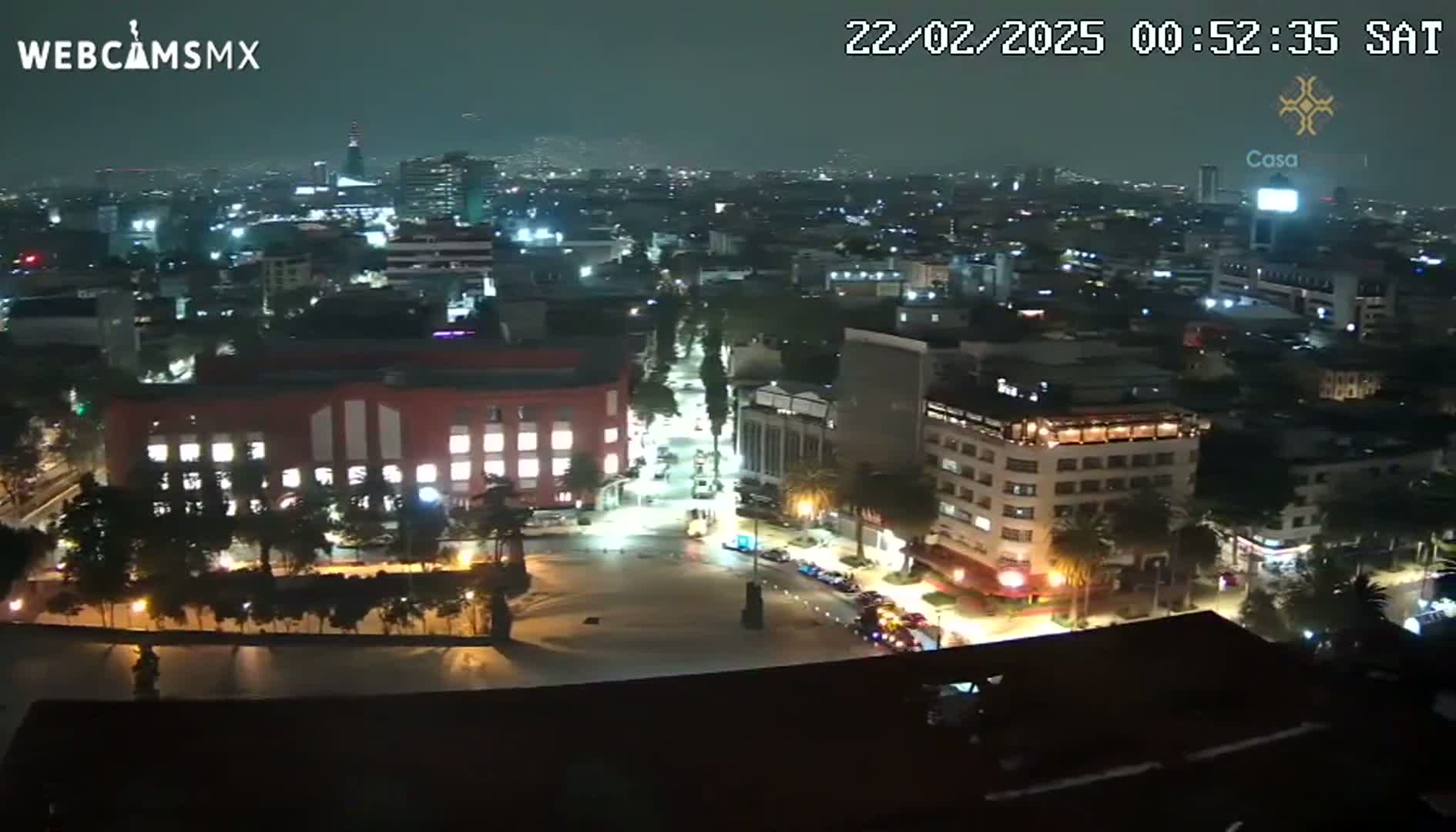 A nighttime aerial view of a city shows illuminated buildings and streets, with a few vehicles visible.