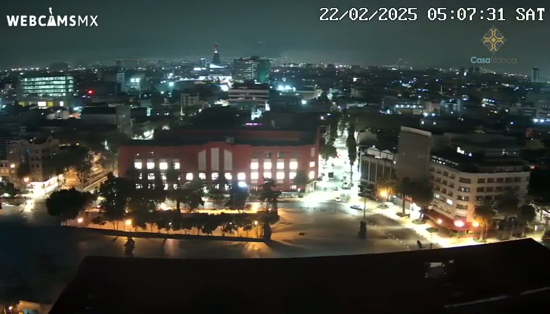 A nighttime aerial view of a city square and surrounding buildings, illuminated by streetlights under a clear, dark sky.