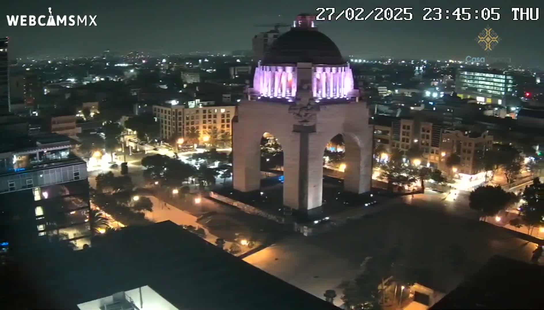 A nighttime, high-angle view of a city illuminated by streetlights, featuring a large monument with a domed top and archway at its center.