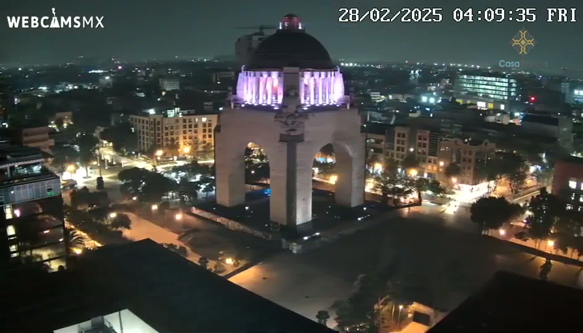 An illuminated monument stands in the center of a nighttime cityscape under a clear sky.
