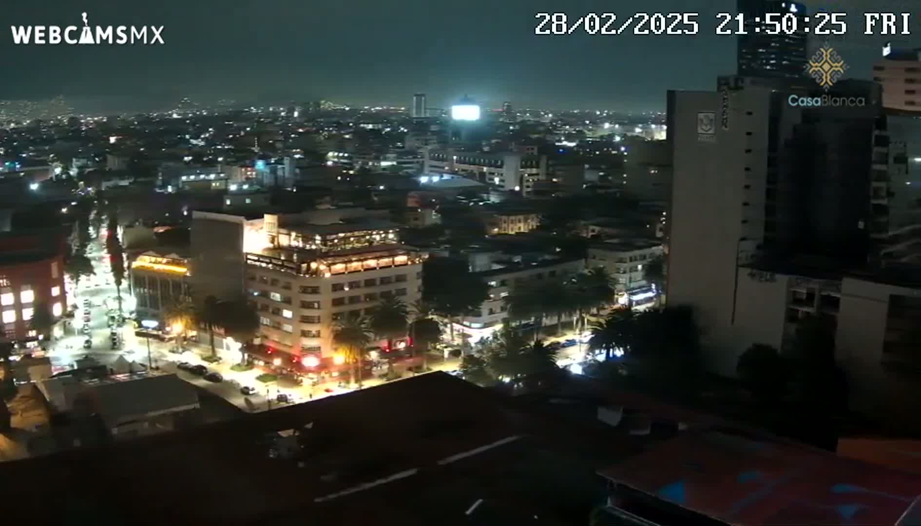 A nighttime, high-angle view of a city with illuminated buildings and streets, showing some vehicle traffic.