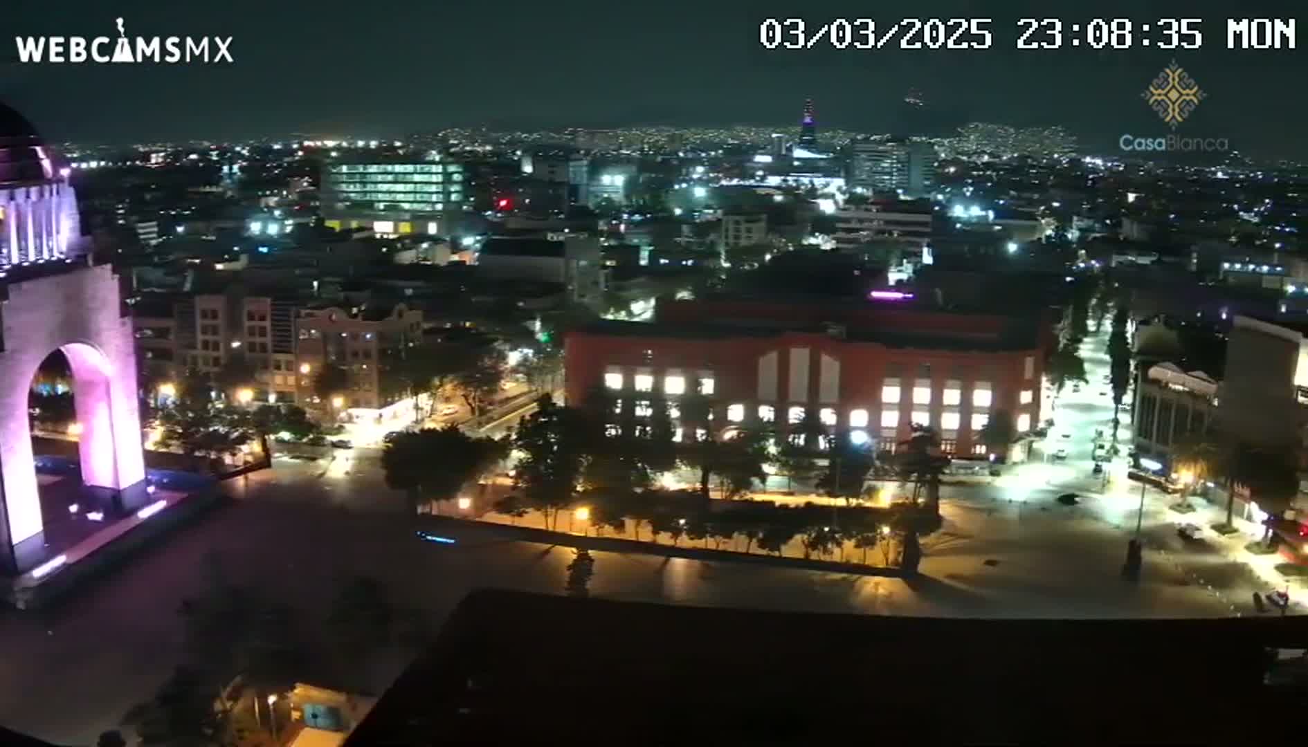 A nighttime, high-angle view of a brightly lit city with a large monument in the foreground.