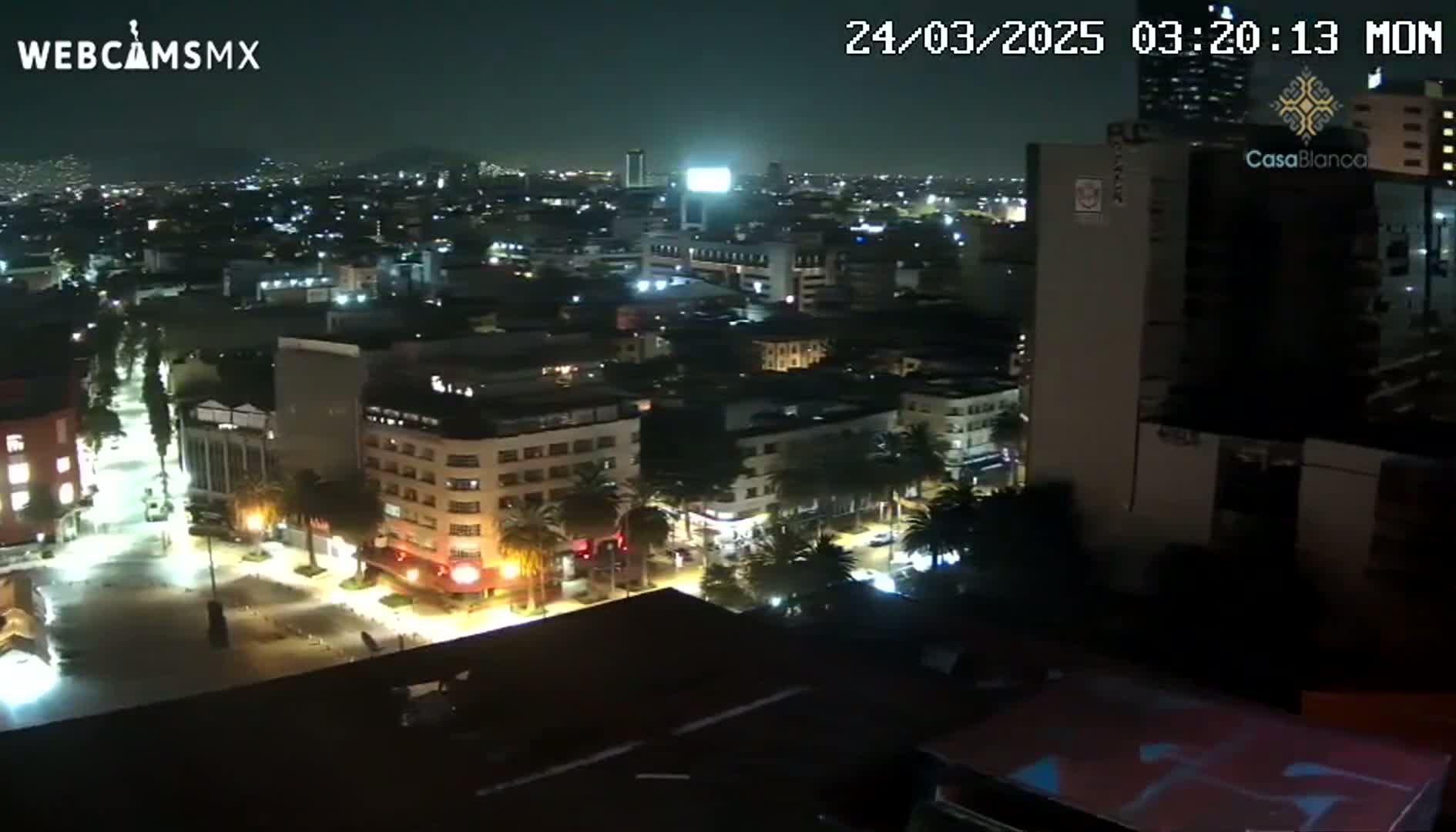 A nighttime aerial view of a city with brightly lit streets and buildings, under clear skies.