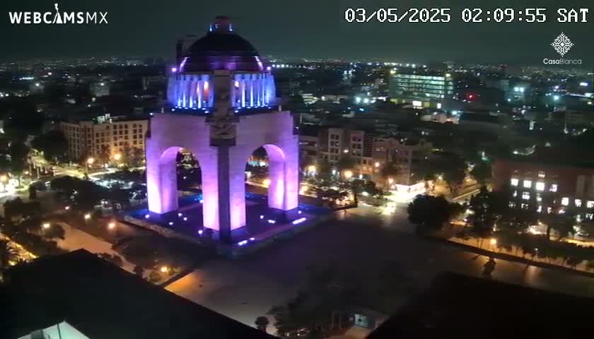 A large monument, illuminated in purple, stands in a city at night.
