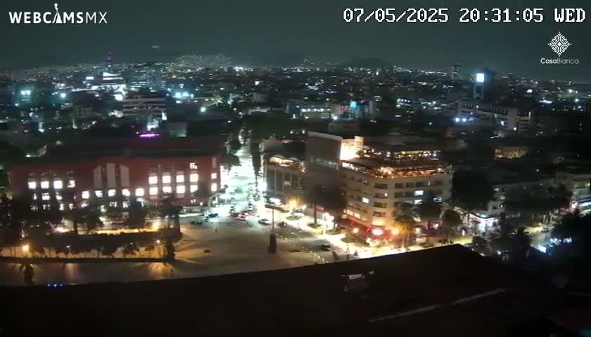A nighttime aerial view of a city shows brightly lit buildings and streets, under a dark, clear sky.