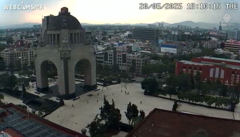 An elevated view shows a large stone monument with an archway in a city square under a partly cloudy evening sky.