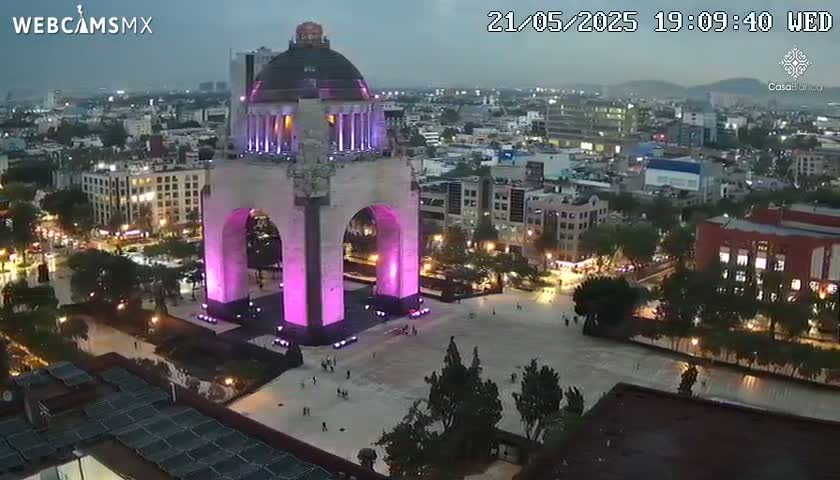 An illuminated monument stands in a city square at night under a cloudy sky.