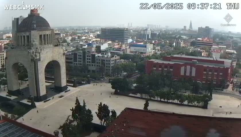 An elevated view shows a large stone monument with an archway in a city square on a hazy day.