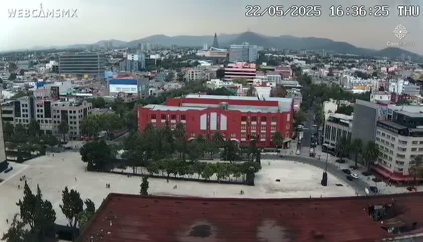 An overcast view of a city square surrounded by buildings, including a large red building, under a hazy sky.