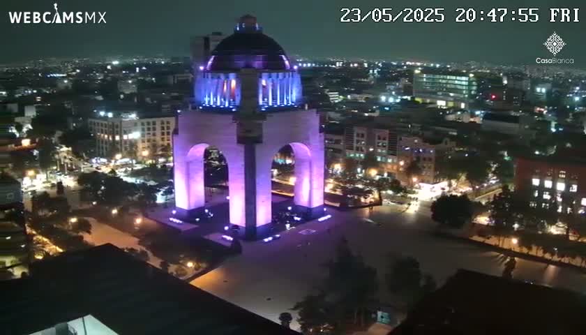 A large, illuminated monument stands in a city square at night, surrounded by buildings and streets with vehicle lights.