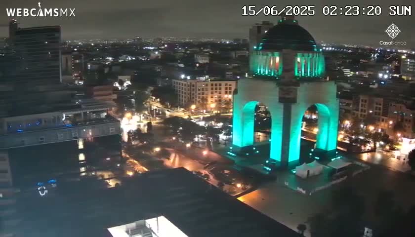 A nighttime, high-angle view of a city featuring a large monument illuminated in teal green light.