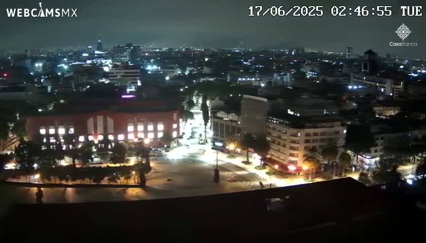 A nighttime aerial view of a city illuminated by streetlights and building lights under a dark, possibly cloudy sky.
