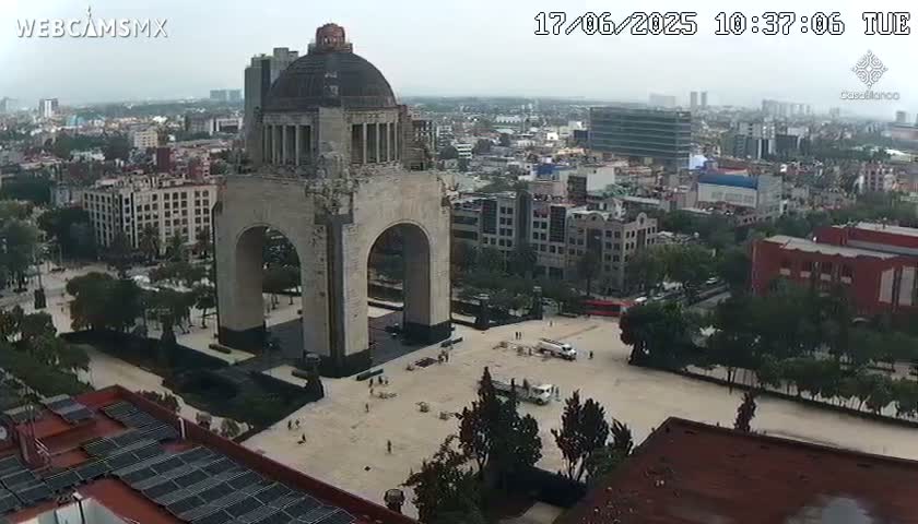 A large stone arch monument stands in a plaza in a city under an overcast sky.
