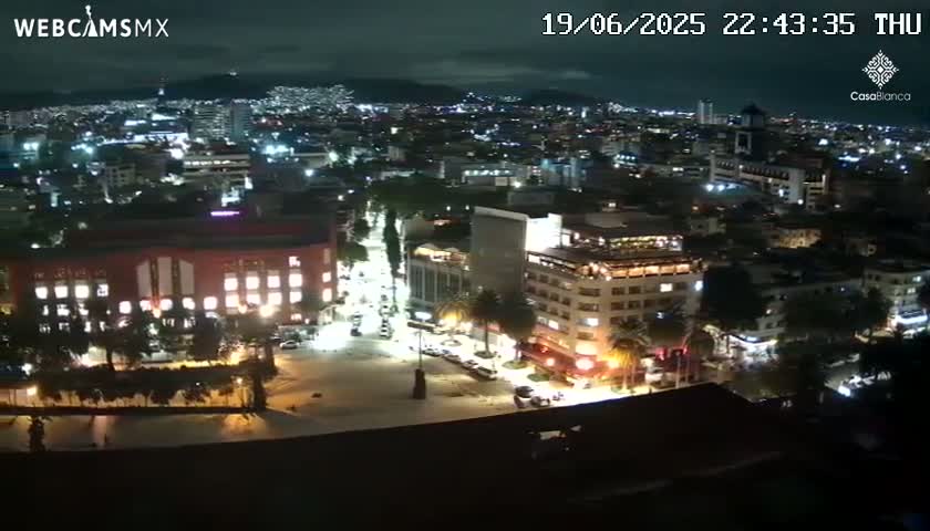 A nighttime, aerial view of a city with brightly lit buildings and streets, under a clear sky.