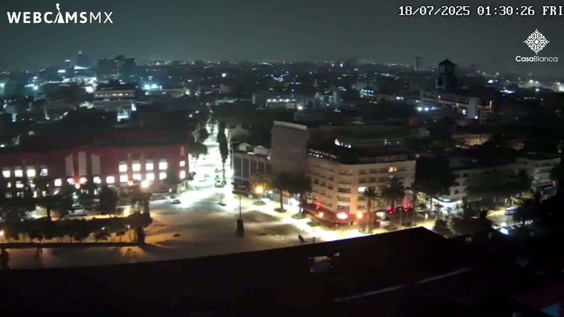 A nighttime aerial view of a city with brightly lit streets and buildings under a hazy sky.