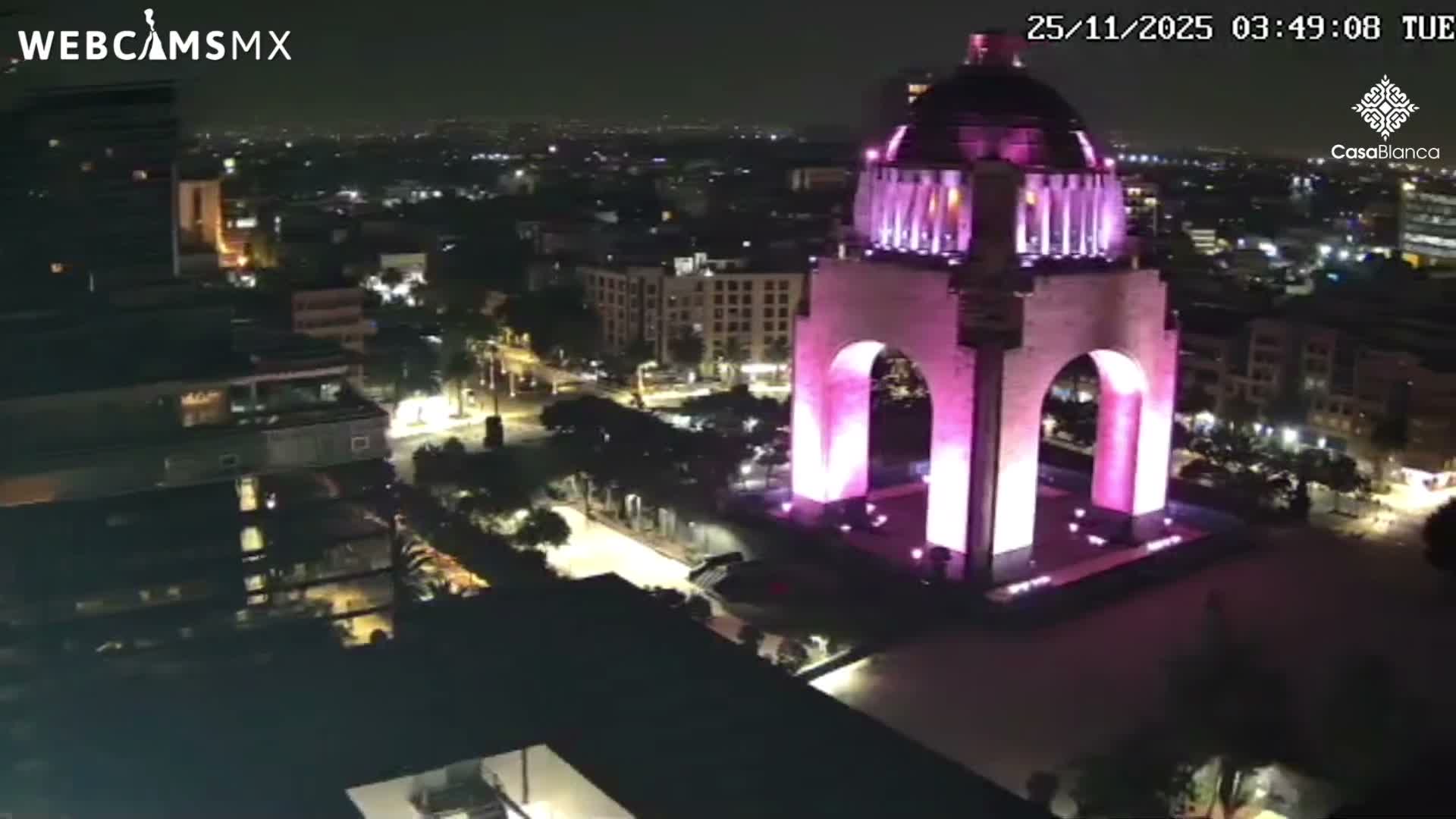 An illuminated monument glowing purple stands prominently in a sprawling city at night under clear skies.