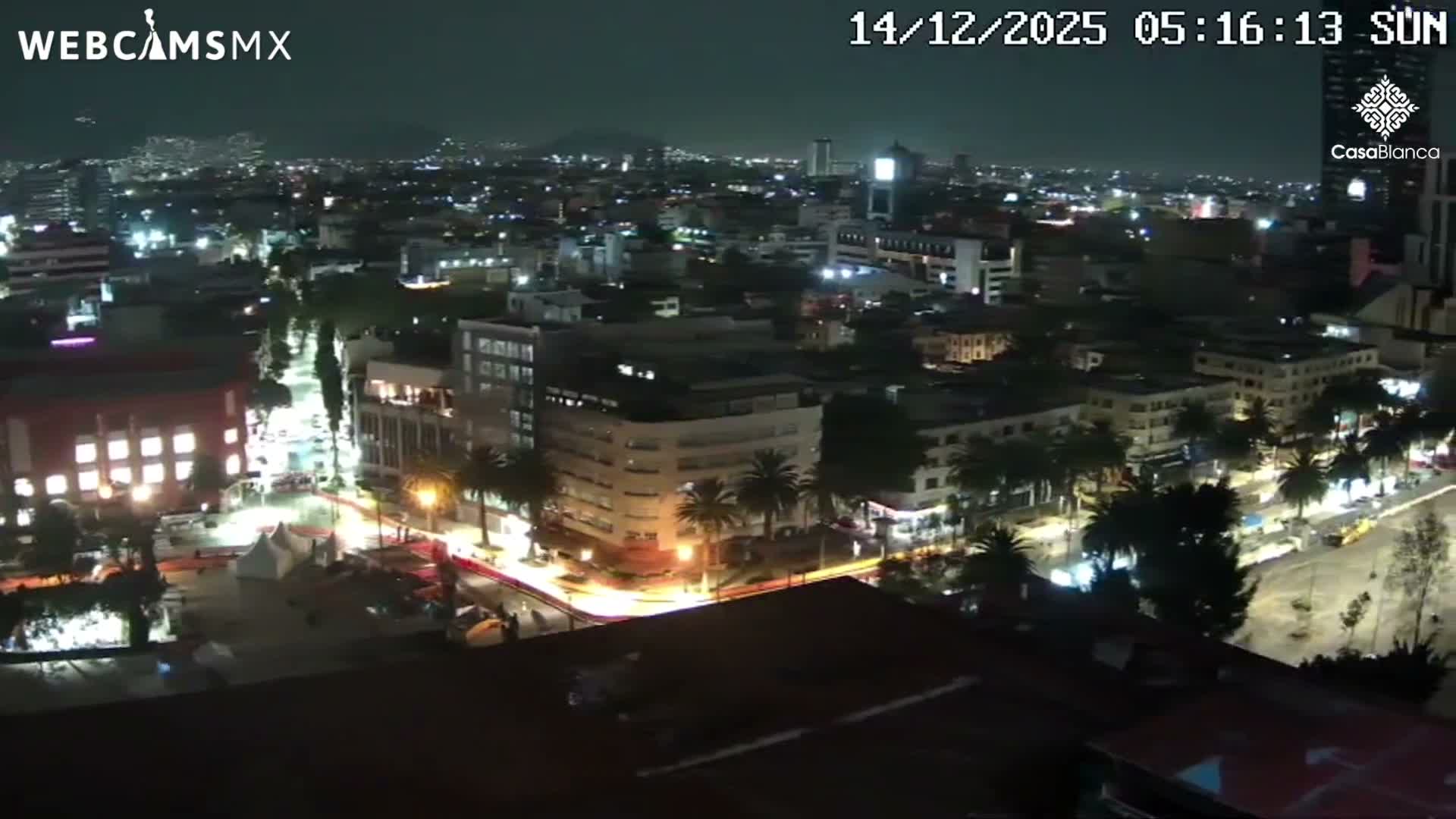 An illuminated monument glowing purple stands prominently in a sprawling city at night under clear skies.