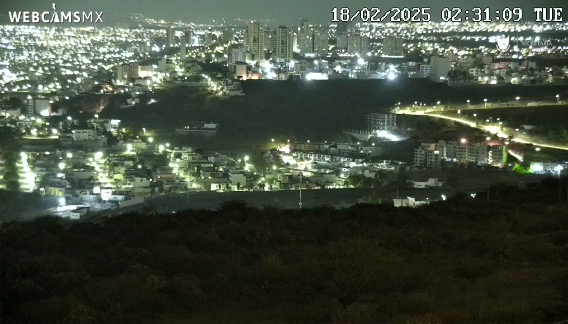 A nighttime, high-angle view of a city sprawling across a hillside, illuminated by numerous lights.