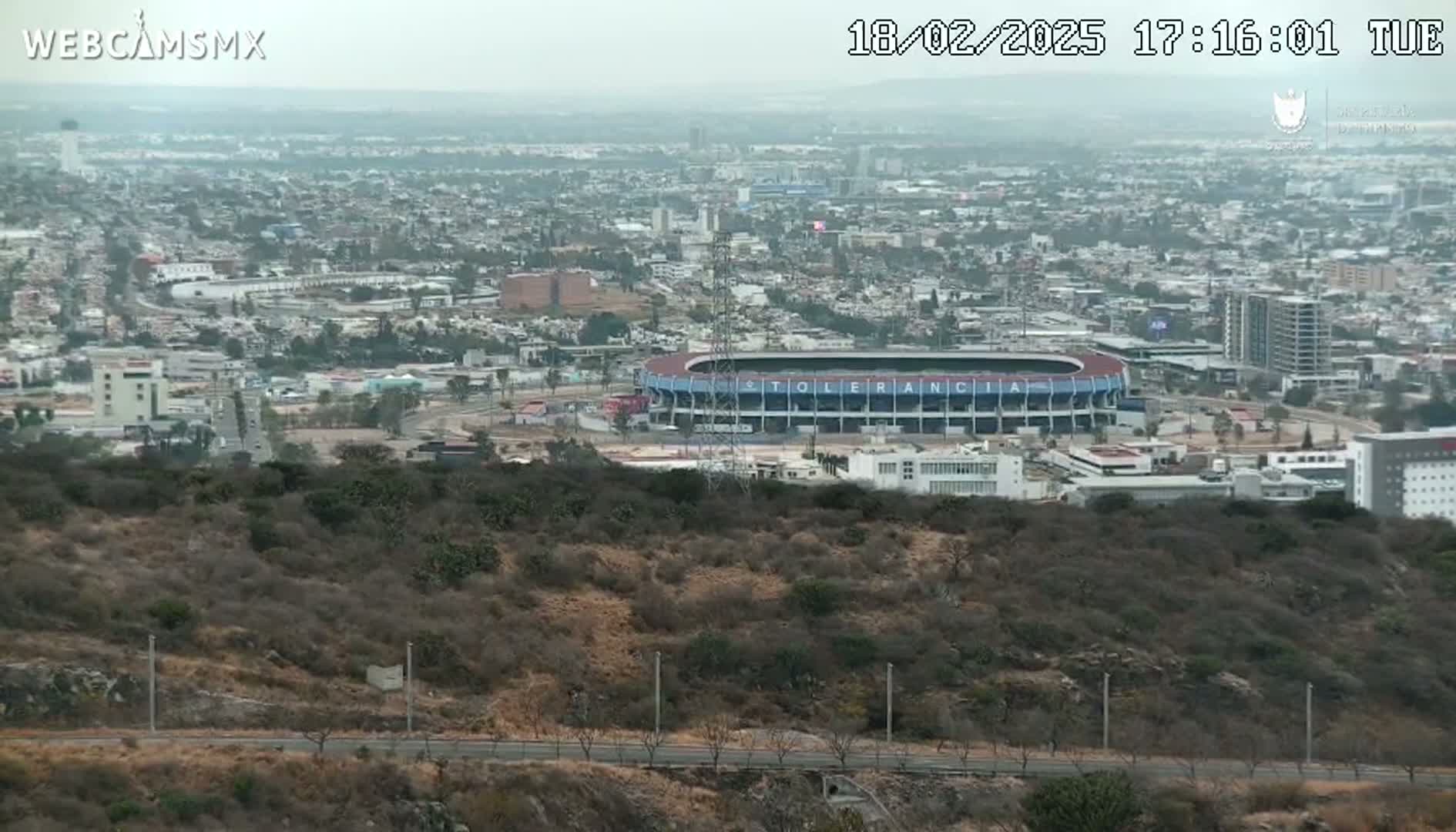 A hazy, long shot of a city with a stadium visible, seen from a hilltop.