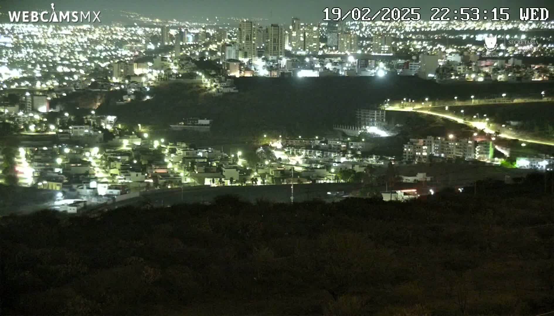 A nighttime view of a city illuminated by streetlights, showing a sprawling landscape of buildings and roads extending towards a distant skyline.