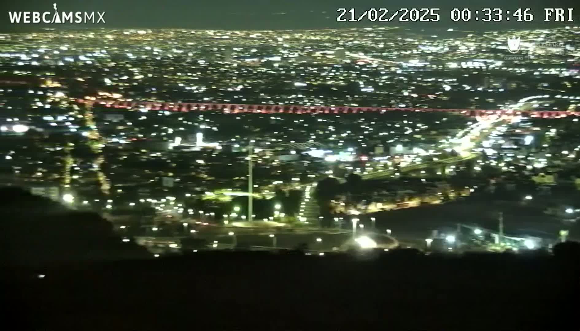 A nighttime, high-angle view of a sprawling city illuminated by countless lights.