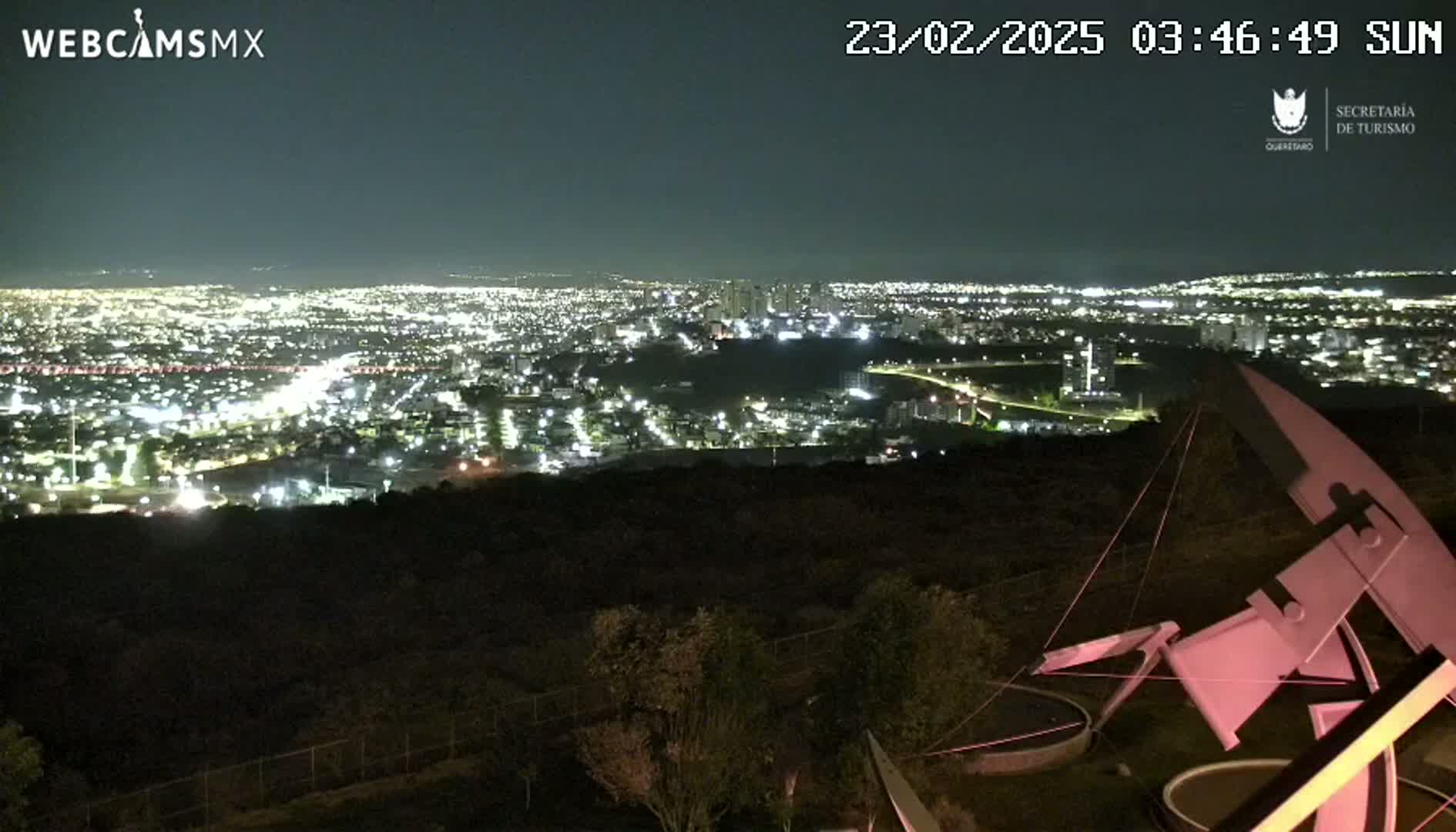 A nighttime view from a hilltop overlooking a sprawling city illuminated by lights, under a clear sky.