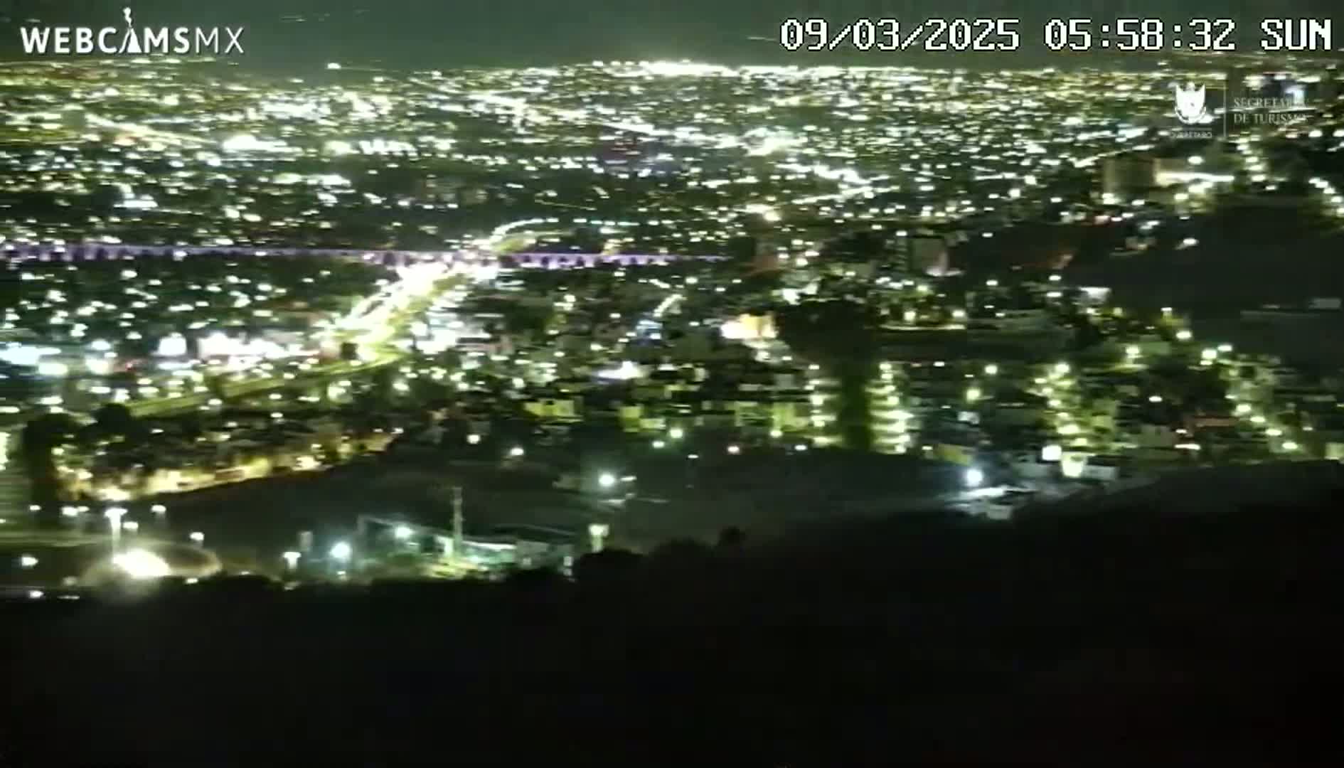 A nighttime, high-angle view shows a sprawling city illuminated by countless lights.