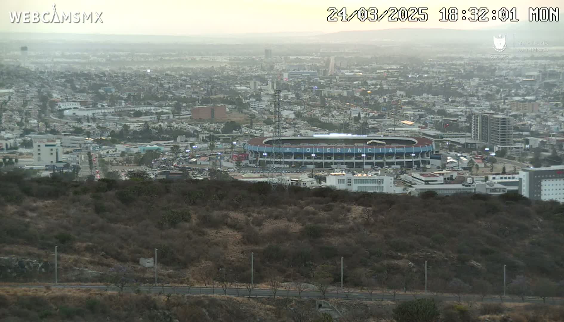 A hazy dusk view overlooking a sprawling city with a stadium and surrounding hills.