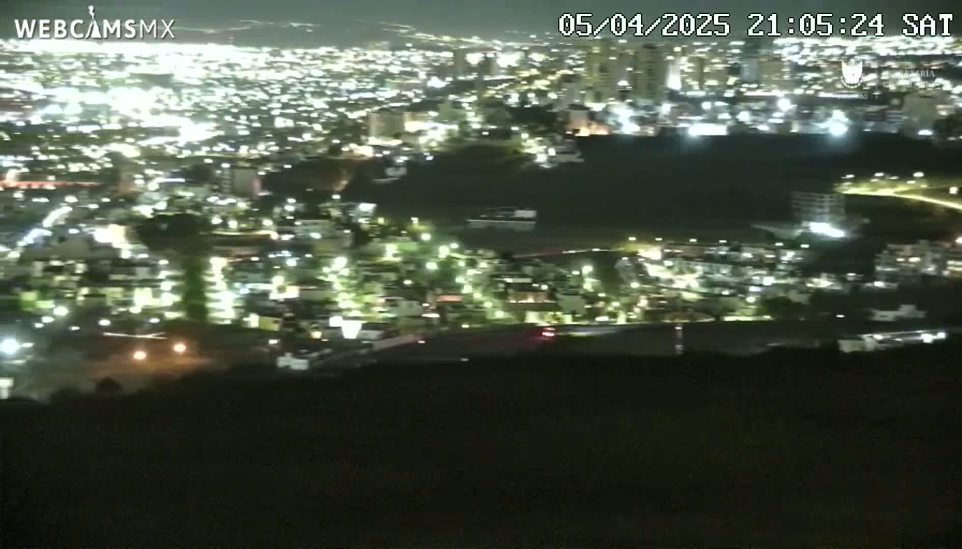 A nighttime, high-angle view shows a sprawling city illuminated by many lights.
