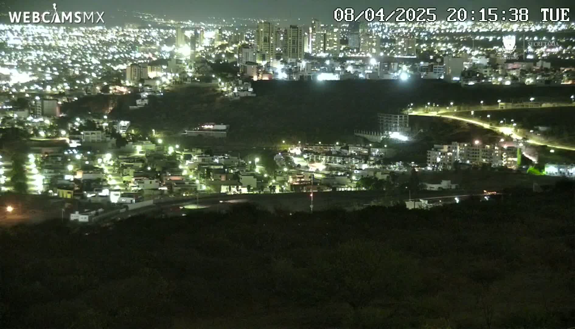 A nighttime, high-angle view of a city illuminated by streetlights, extending into the distance and nestled against a dark hillside.