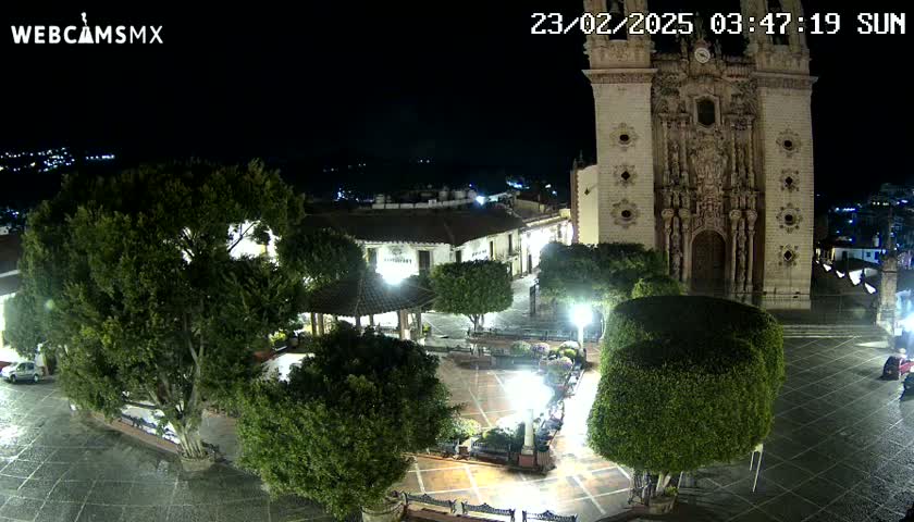 A nighttime view of a town square with a large church, trees, and outdoor lighting.