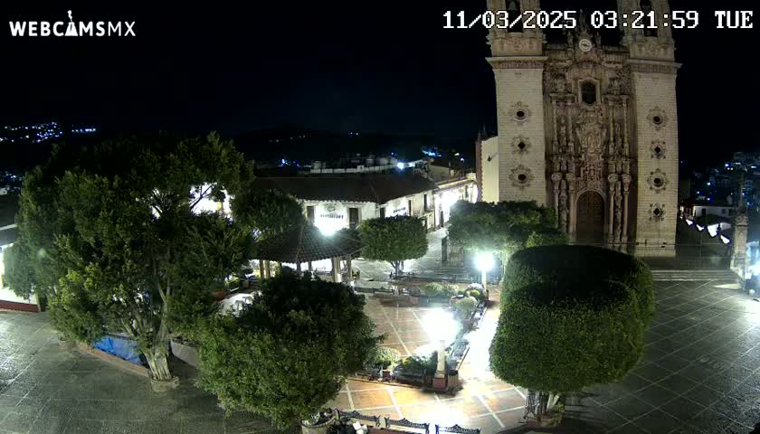 A nighttime, high-angle view of a town square with a large church, several trees, and a gazebo, under a clear, dark sky.