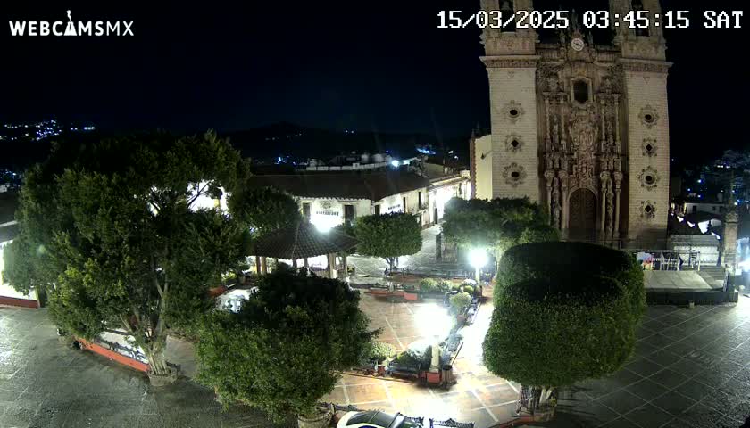 A nighttime view of a town square with a large church, several trees, and a gazebo, under clear skies.