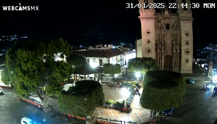 A nighttime view of a town square with a large church, several trees, and some people.