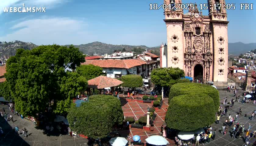 A town square with a large church and several people, under a sunny sky with mountains in the distance.