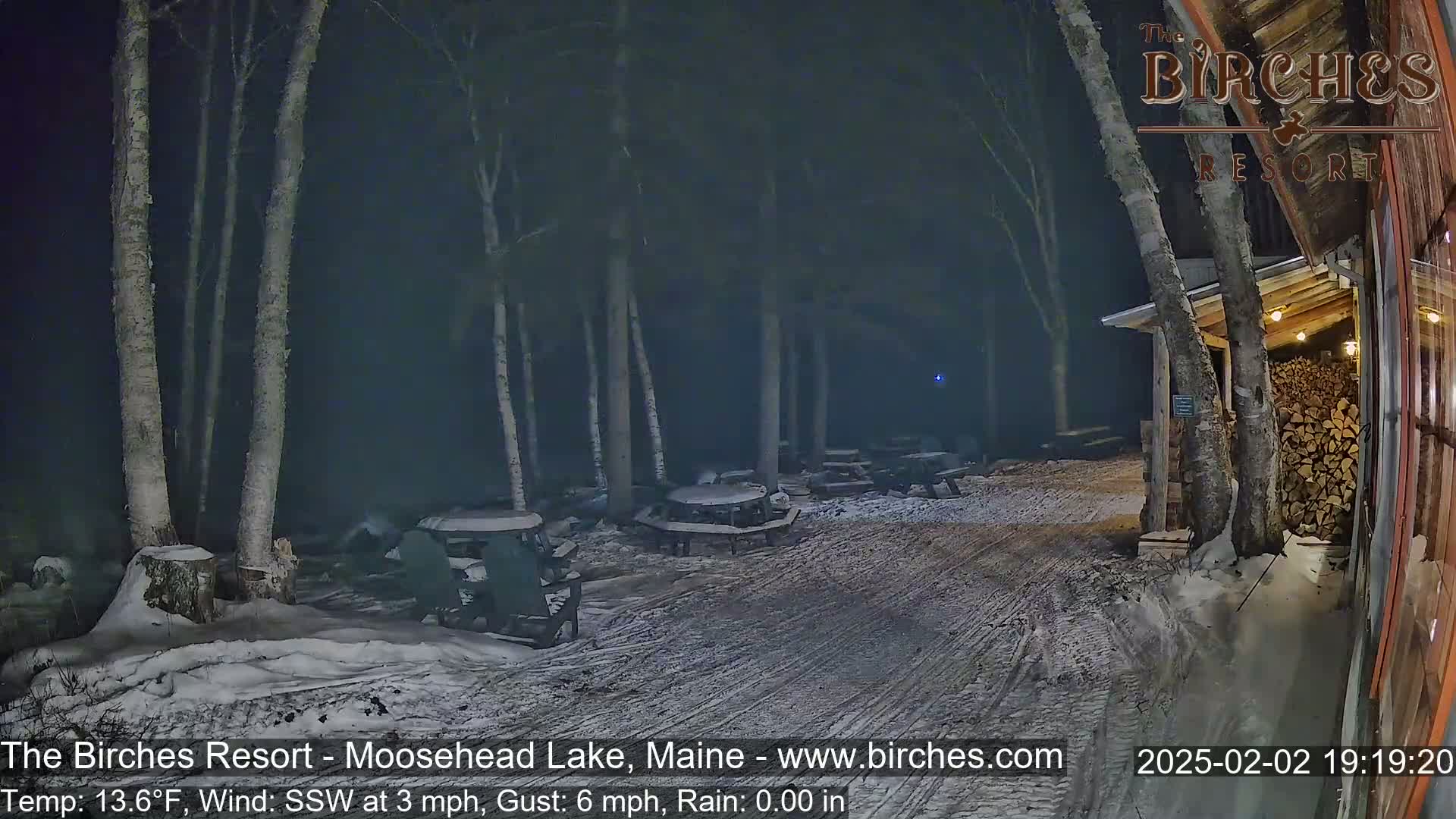 A snow-covered outdoor patio area with picnic tables and chairs is visible at night under a dark, rainy sky.