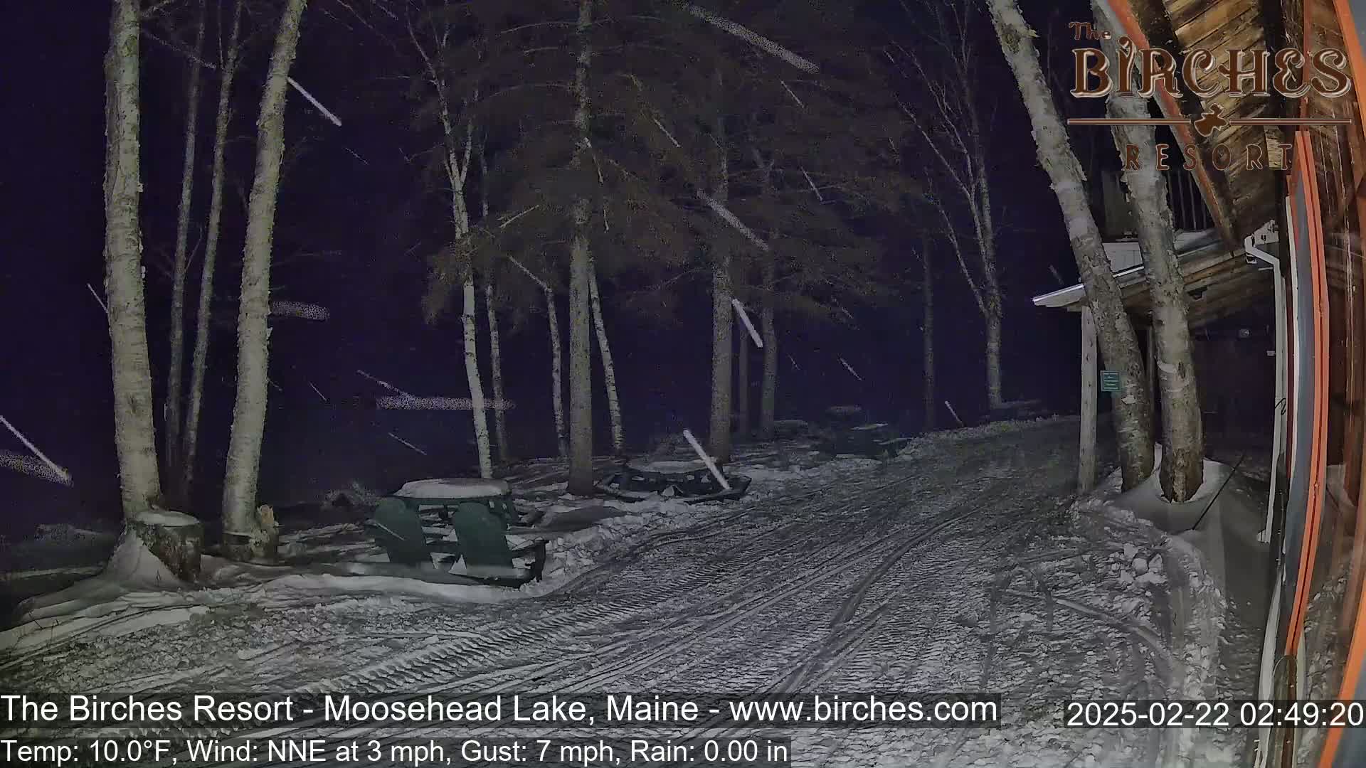 A snow-covered picnic area with a building in the background during a nighttime snowfall.