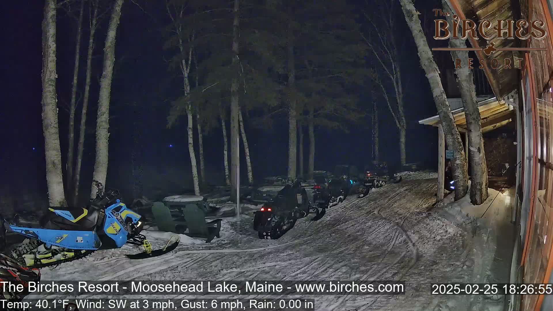 Several snowmobiles are parked in a snowy area next to a building at night under a dark sky.