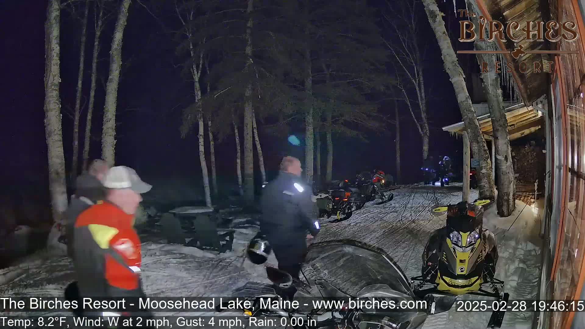 Several people are arriving at a snowmobile resort at night in snowy conditions with a westerly wind of 2 mph and gusts up to 4 mph, and the temperature is 8.2°F.