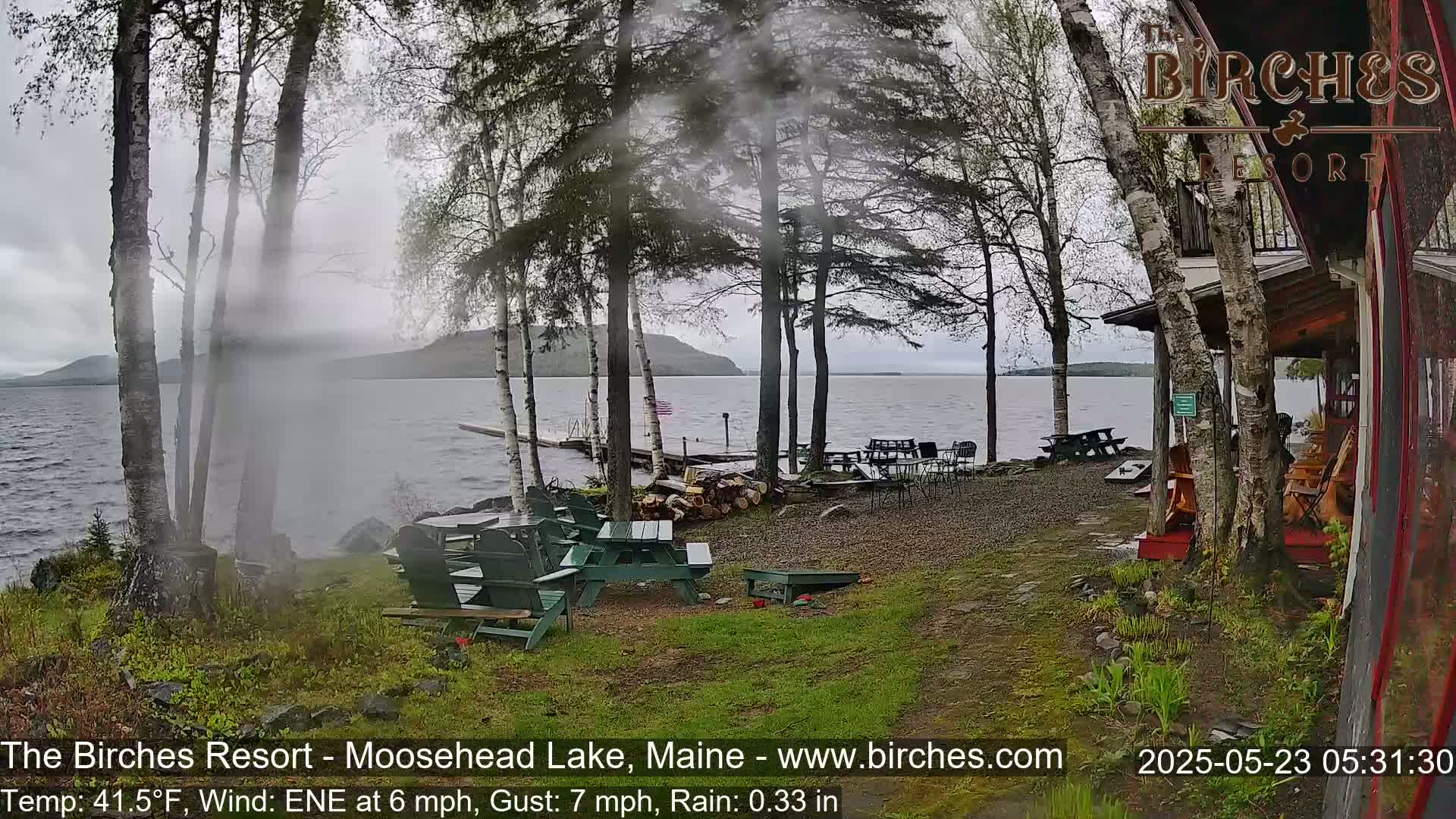 A lakeside resort with outdoor seating under a misty, rainy sky.