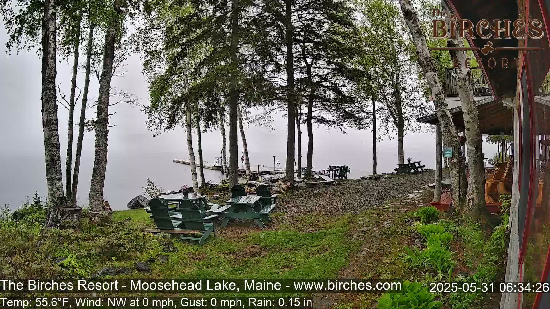 A lakeside resort area with picnic tables and chairs under a misty, rainy sky.