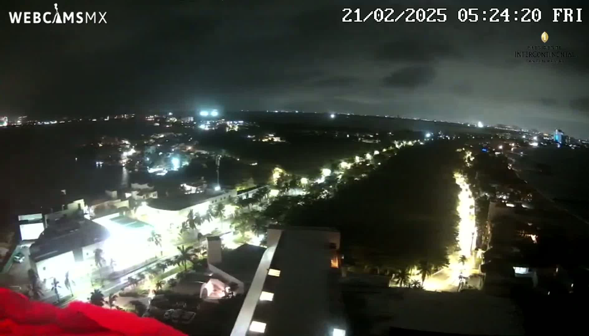 A nighttime, high-angle view shows a city with illuminated streets and buildings, under a mostly clear sky.