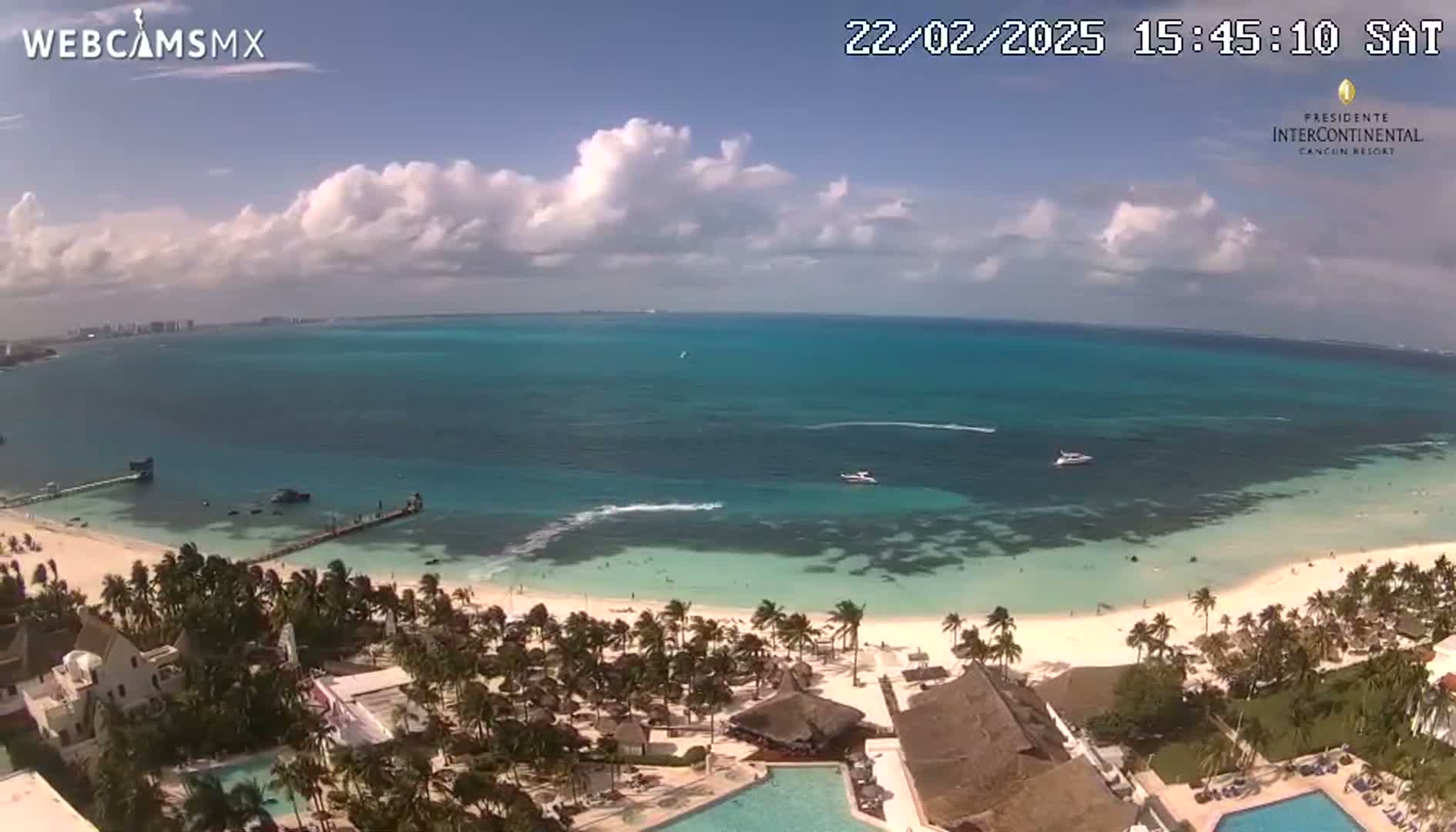 A partly cloudy day overlooking a tropical beach with turquoise water, palm trees, and a resort.