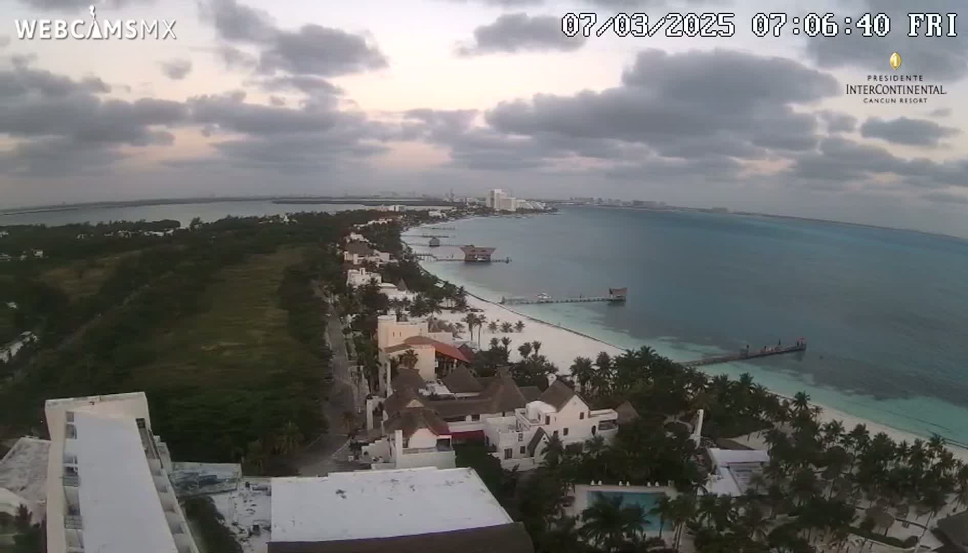 An aerial view of a coastal resort town on a cloudy morning, showing a long stretch of beach, ocean, and buildings.