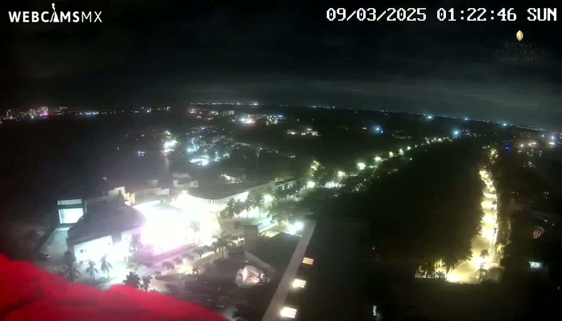 A nighttime aerial view shows a city with illuminated buildings and streets, under a clear sky.