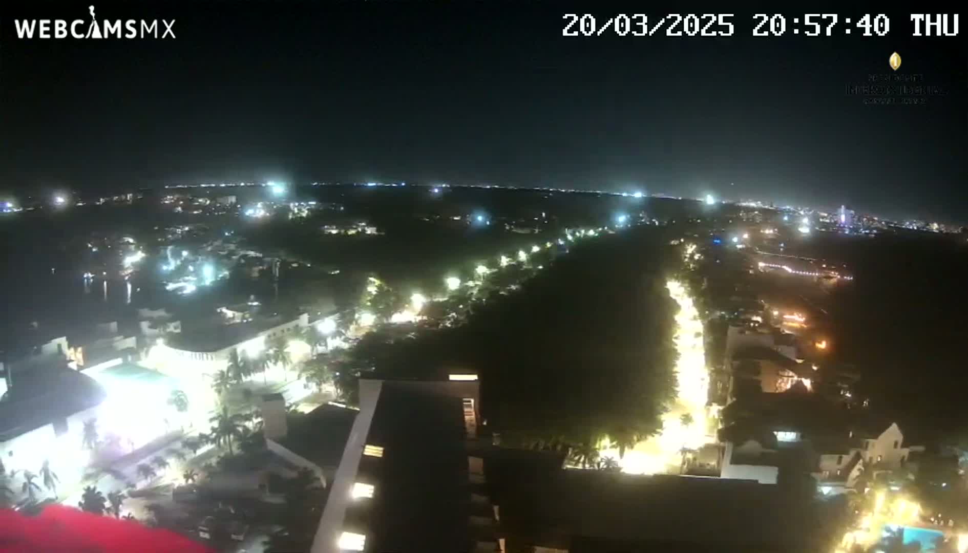 A nighttime, high-angle view shows a city illuminated by streetlights and building lights, with a dark, tree-lined area separating the lit areas.