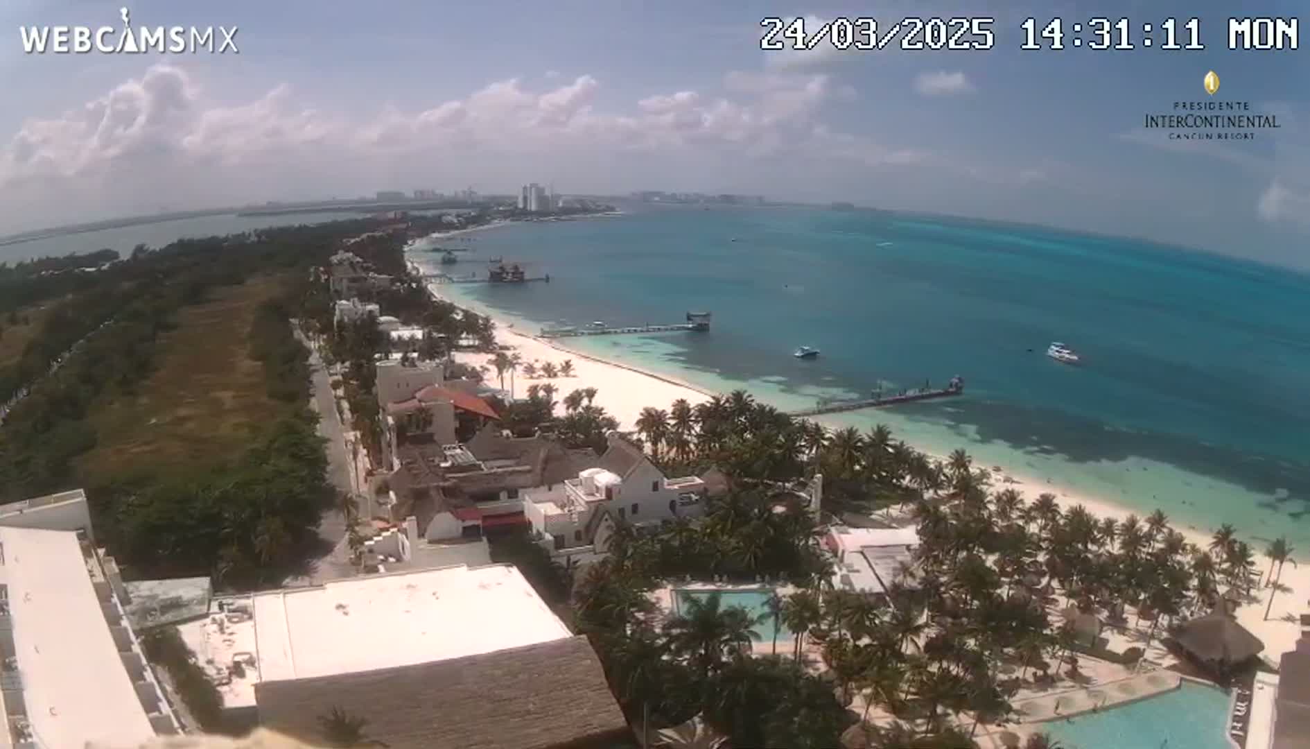 A partly cloudy day overlooking a tropical beach with turquoise water, palm trees, and beachside buildings.