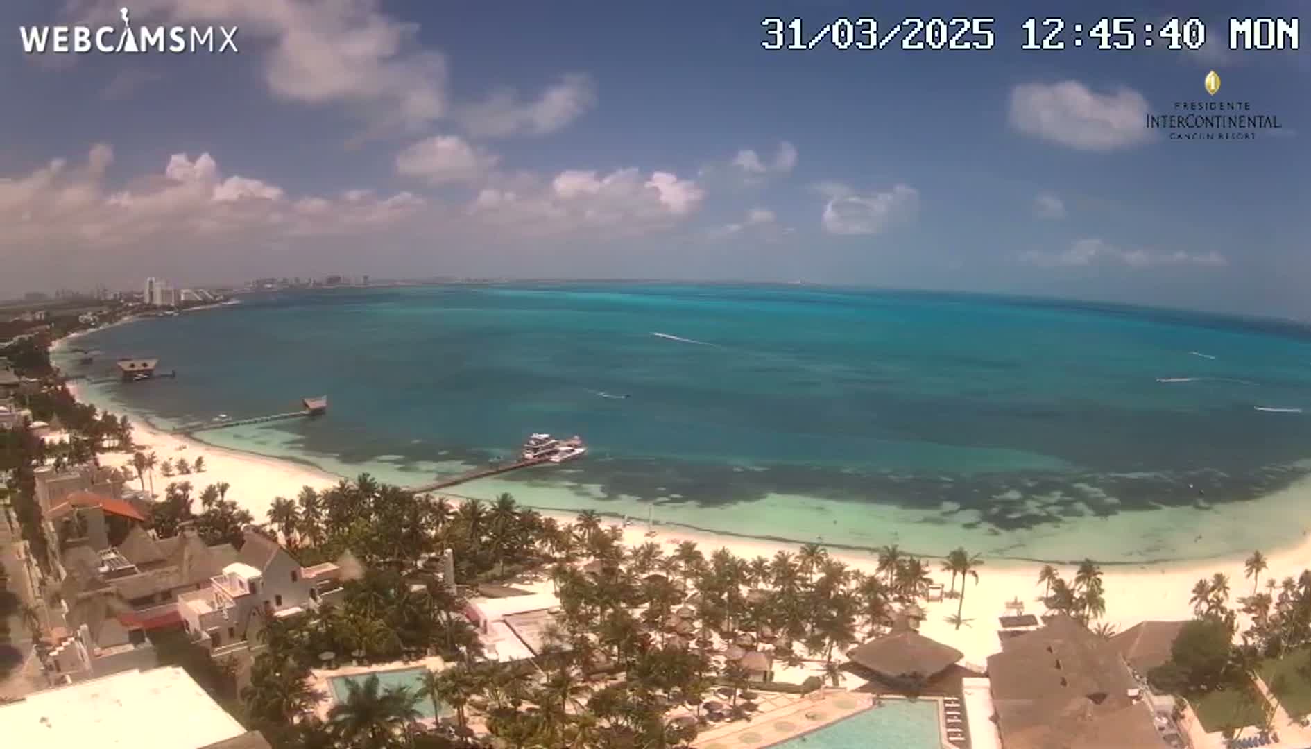 A partly cloudy day reveals a tropical beach scene with turquoise water, white sand, palm trees, and resort buildings.