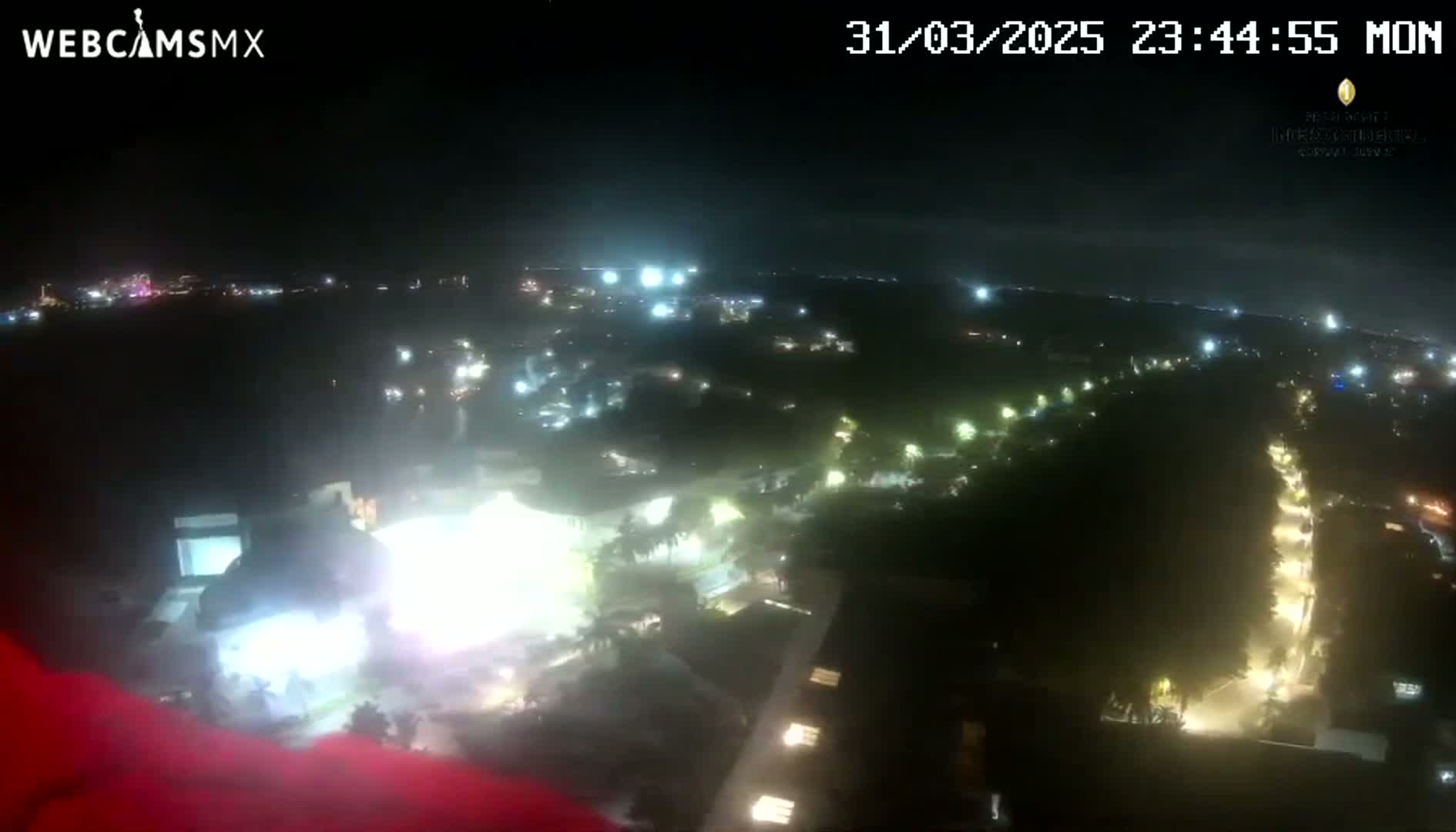 A nighttime, high-angle view shows a sprawling area with numerous lights illuminating buildings and streets, set against a dark sky.