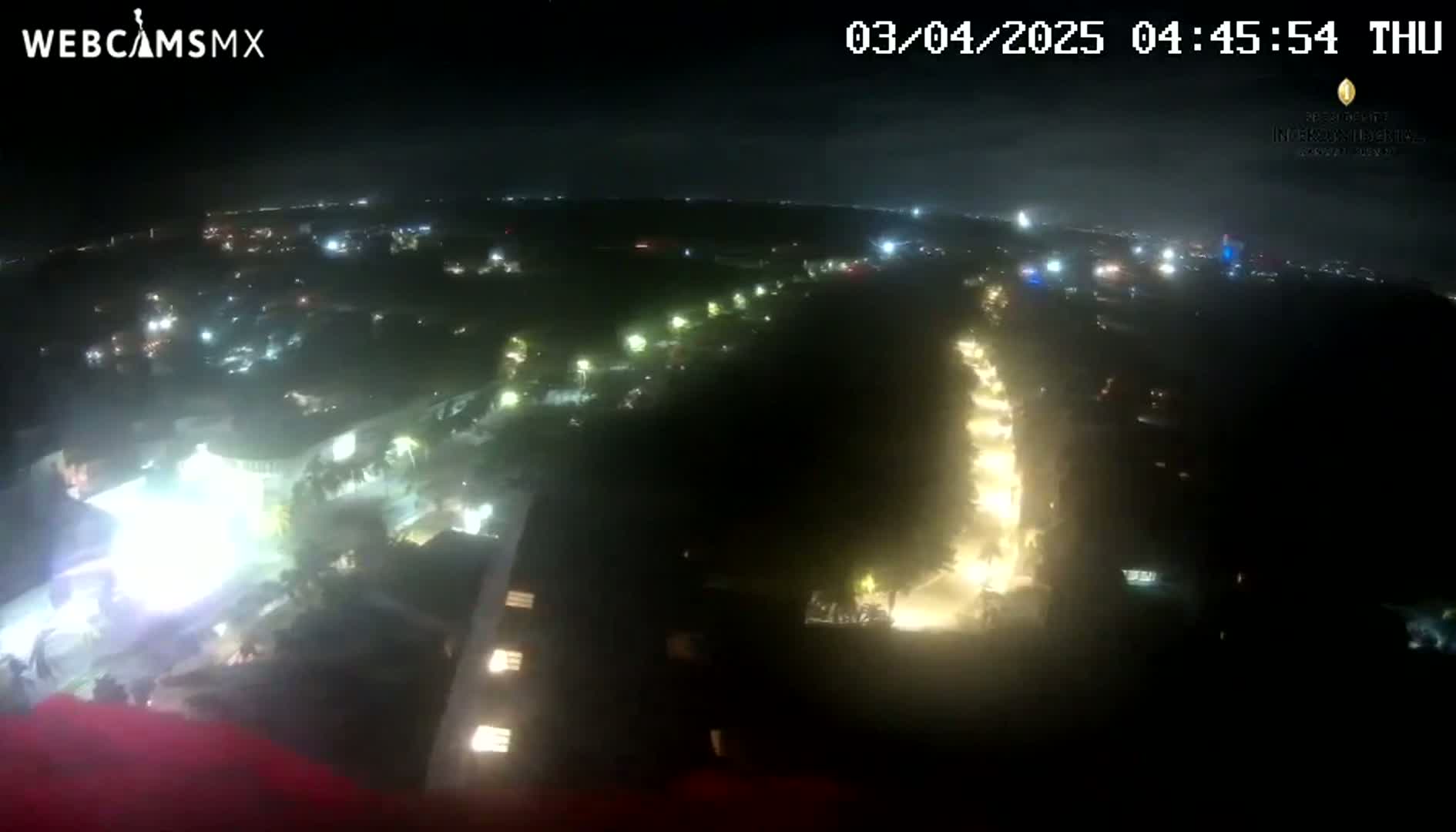 A nighttime aerial view shows a dark landscape with illuminated roads and buildings under a clear sky.